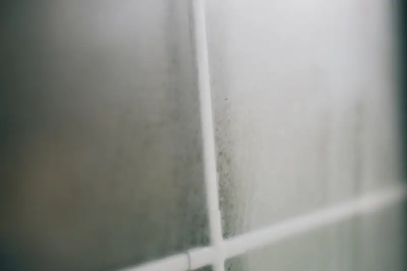 Window glass fogged with beads of condensation behind a white painted frame