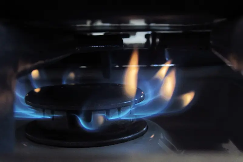 Ring of blue gas flames with yellow tips burning on a kitchen range burner, the same fuel that is scented so a leak can be noticed