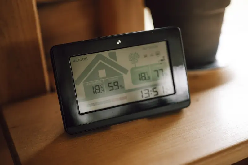 Small digital climate display on a wooden shelf reading indoor and outdoor temperature alongside humidity
